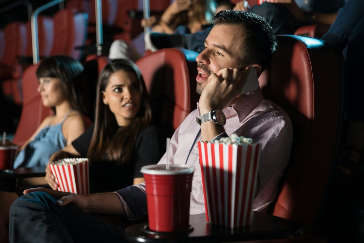 An arrogant man thinking he is the center of the universe using his phone in a full cinema