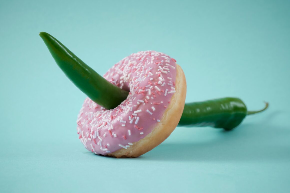 A donut with a long green chili going through the hole in the middle