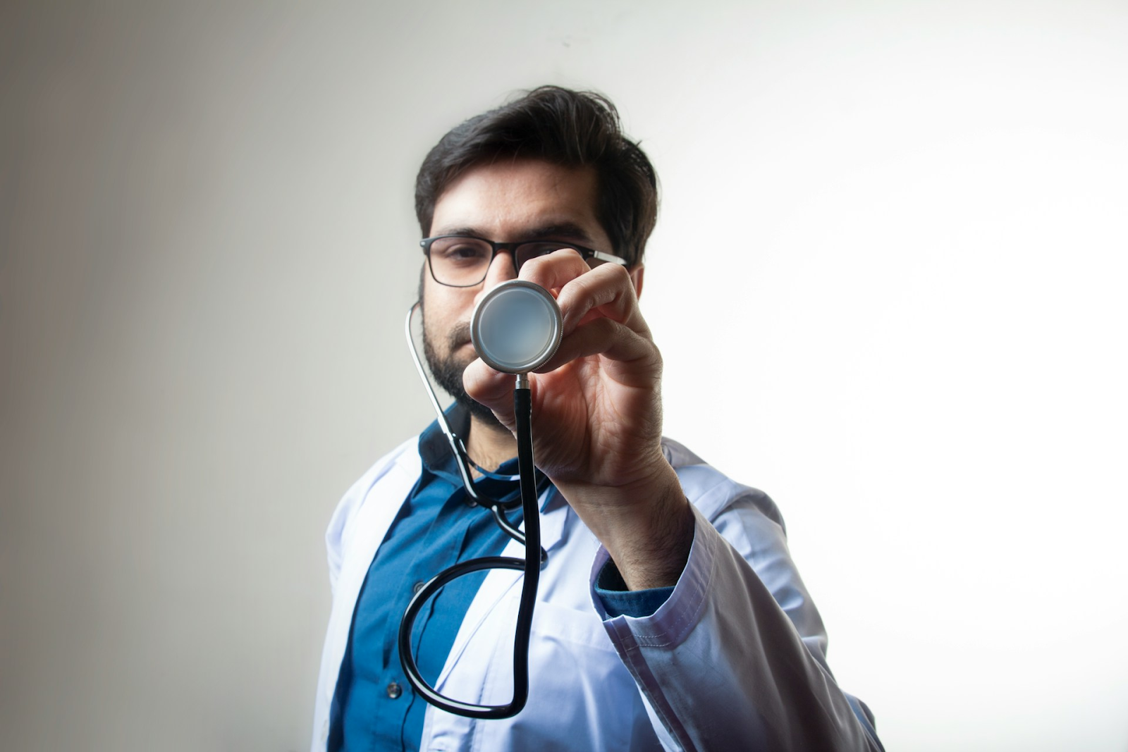 A doctor holding his scope up to the camera in the centre - https://unsplash.com/photos/person-in-white-shirt-holding-black-and-silver-headphones-atn5XAZtRYE