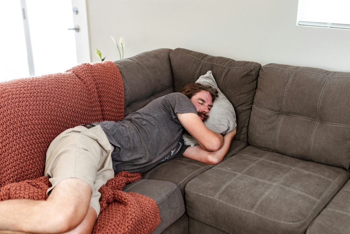 A man sleeping fully clothed on a couch - not ideal for proper sleep