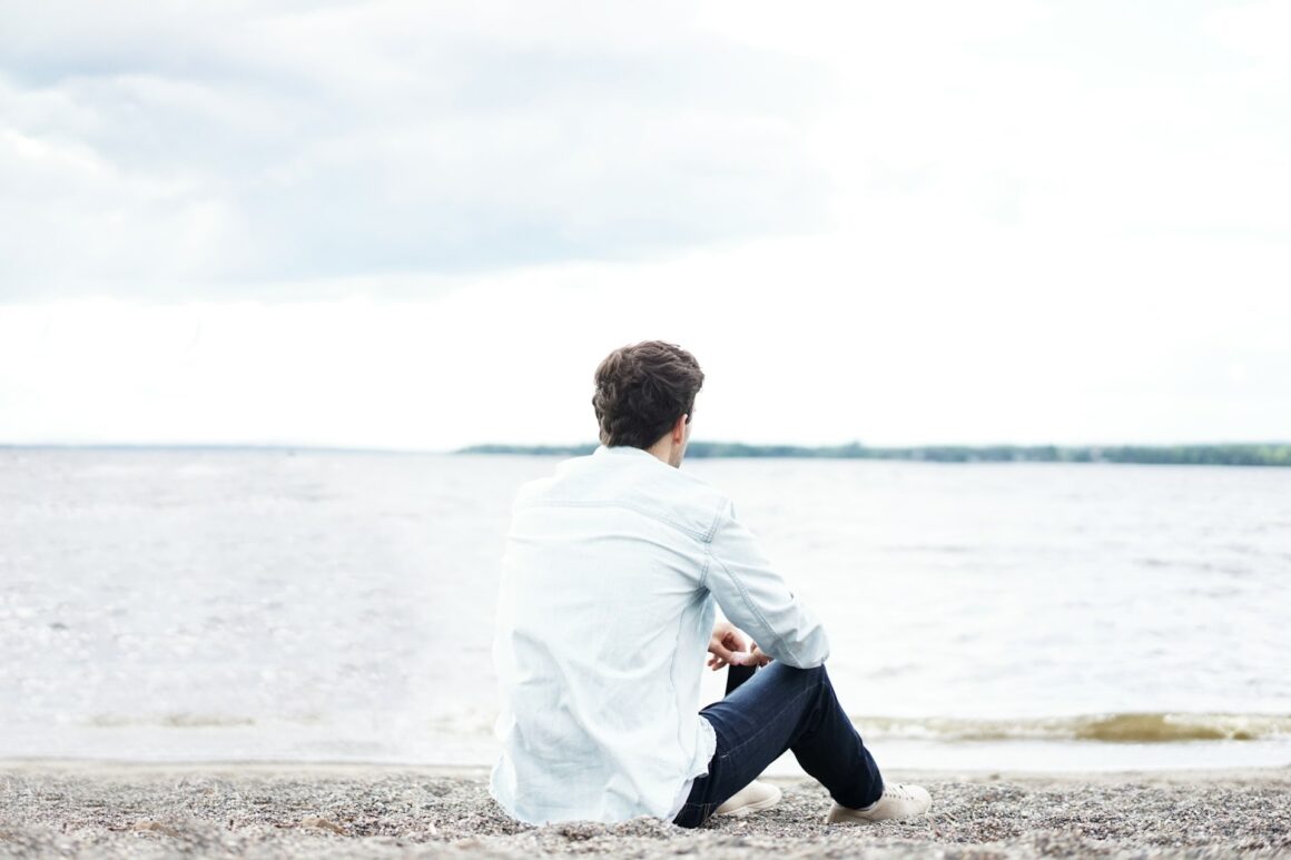 A man sits quietly on a beach contemplating his life decisions.