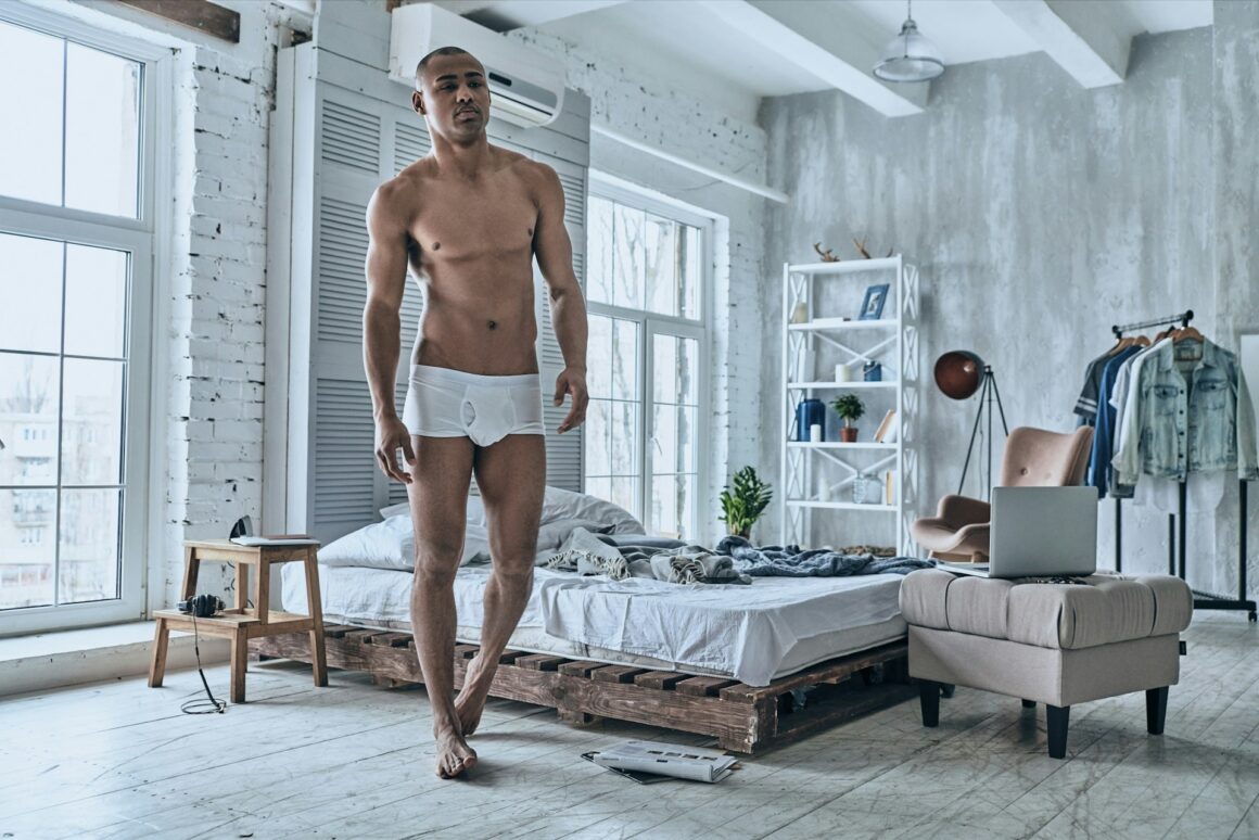 A man walking through a white modern bedroom in just white boxer briefs