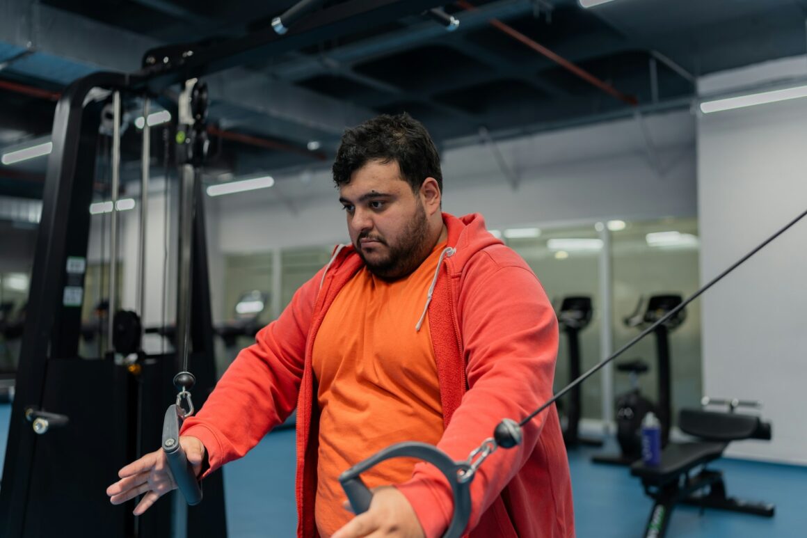 A larger guy in an orange hoodie working out in the gym