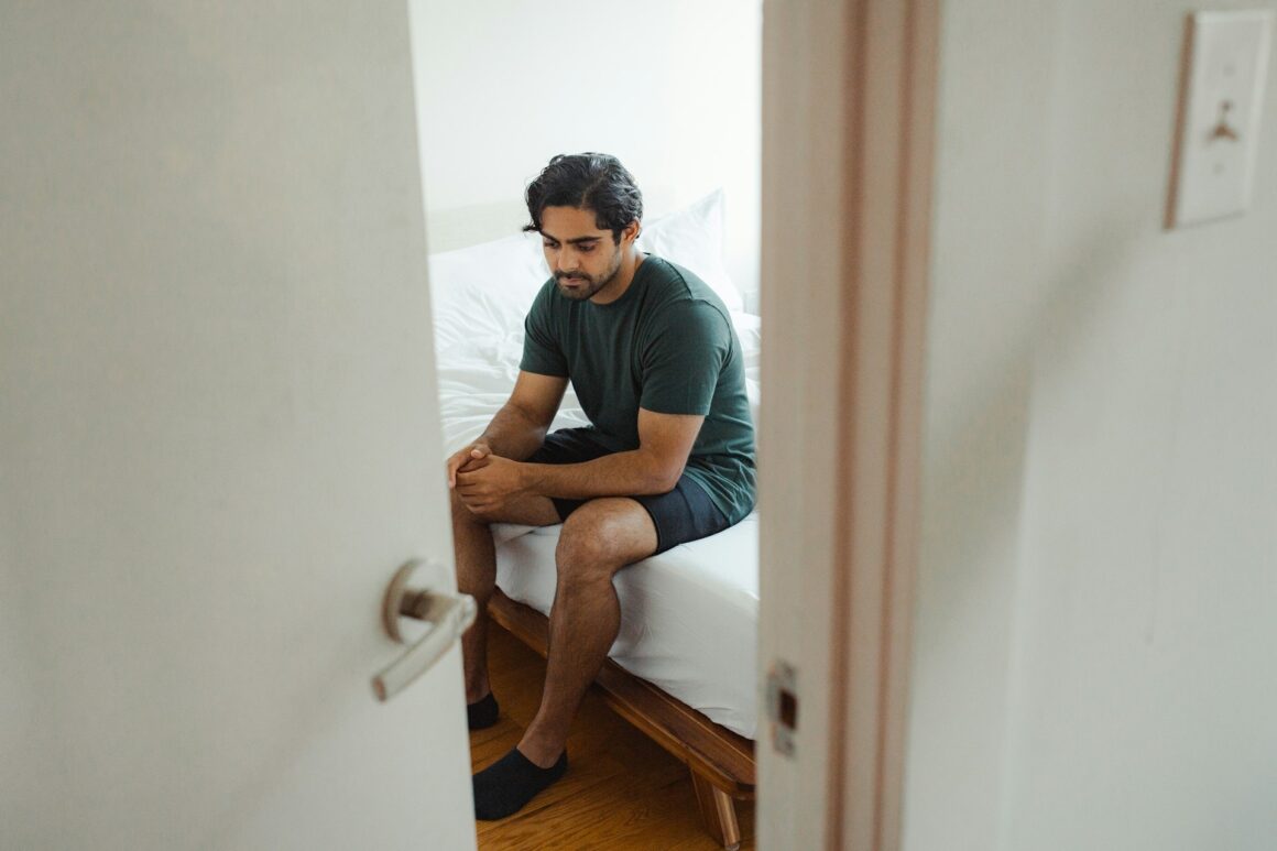 A man sits sadly on the edge of his bed after not being able to get an erection due to excessive tobacco exposure