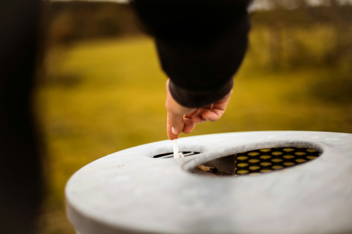 A man stubbing out a cigarette on an outdoor bin, giving up for good