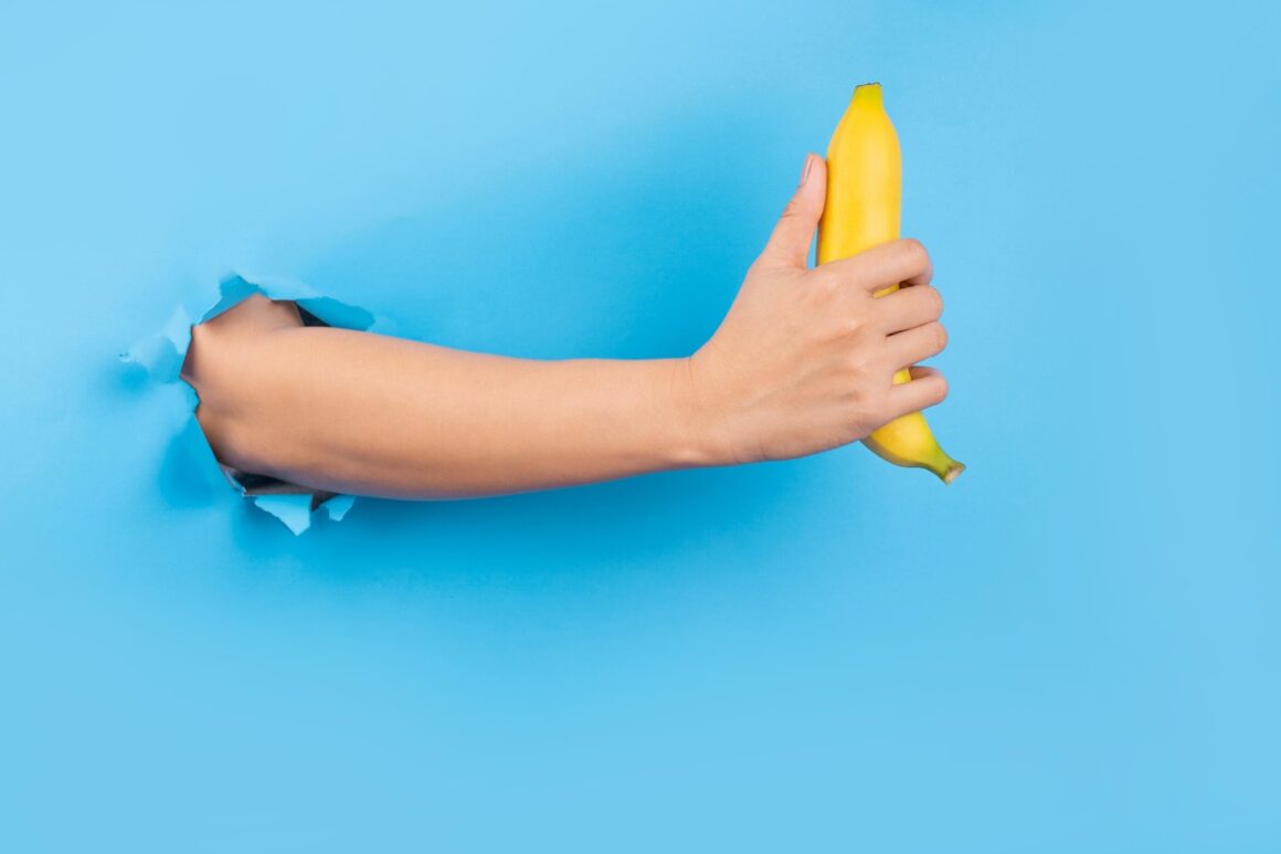 Hand through paper holding banana on blue background