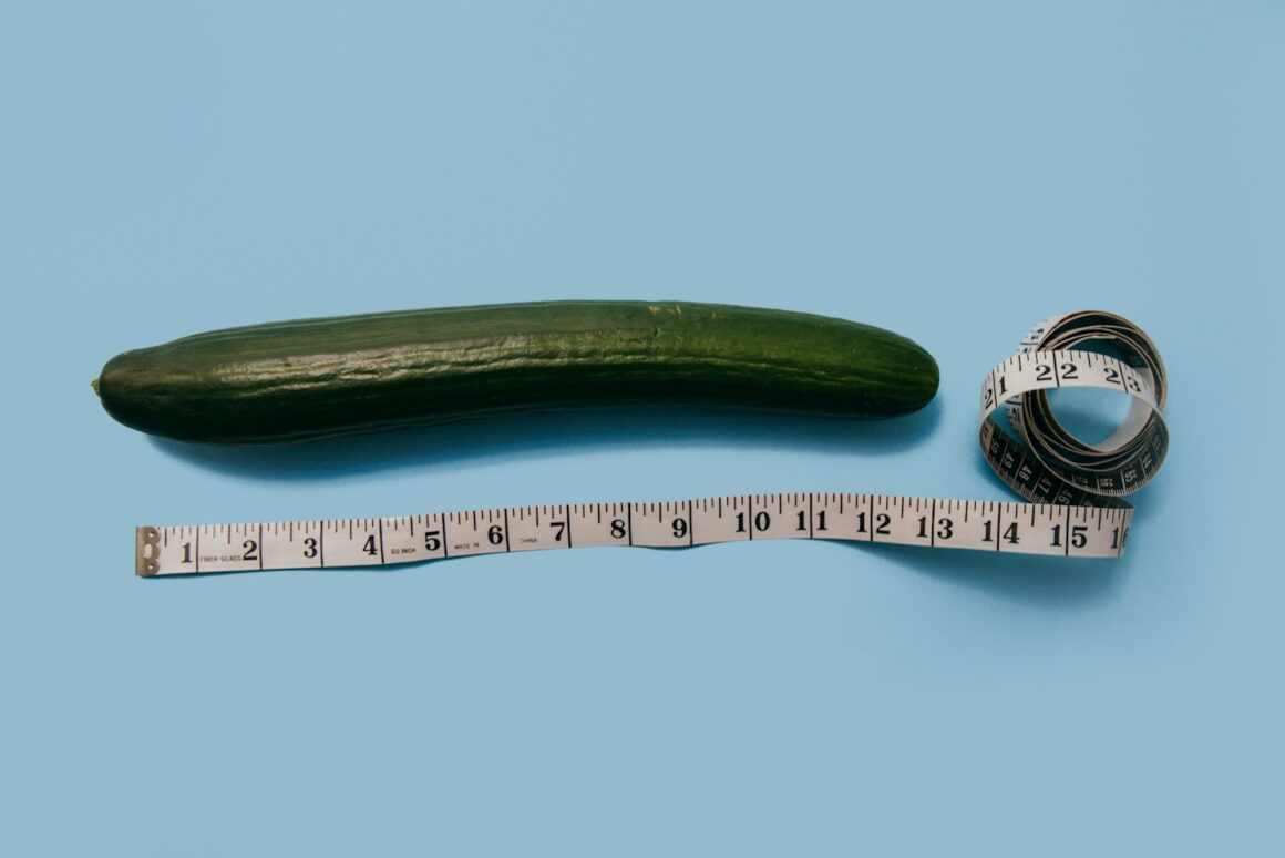 A cucumber of a blue aesthetic background next to a tape measure to represent measuring a penis size