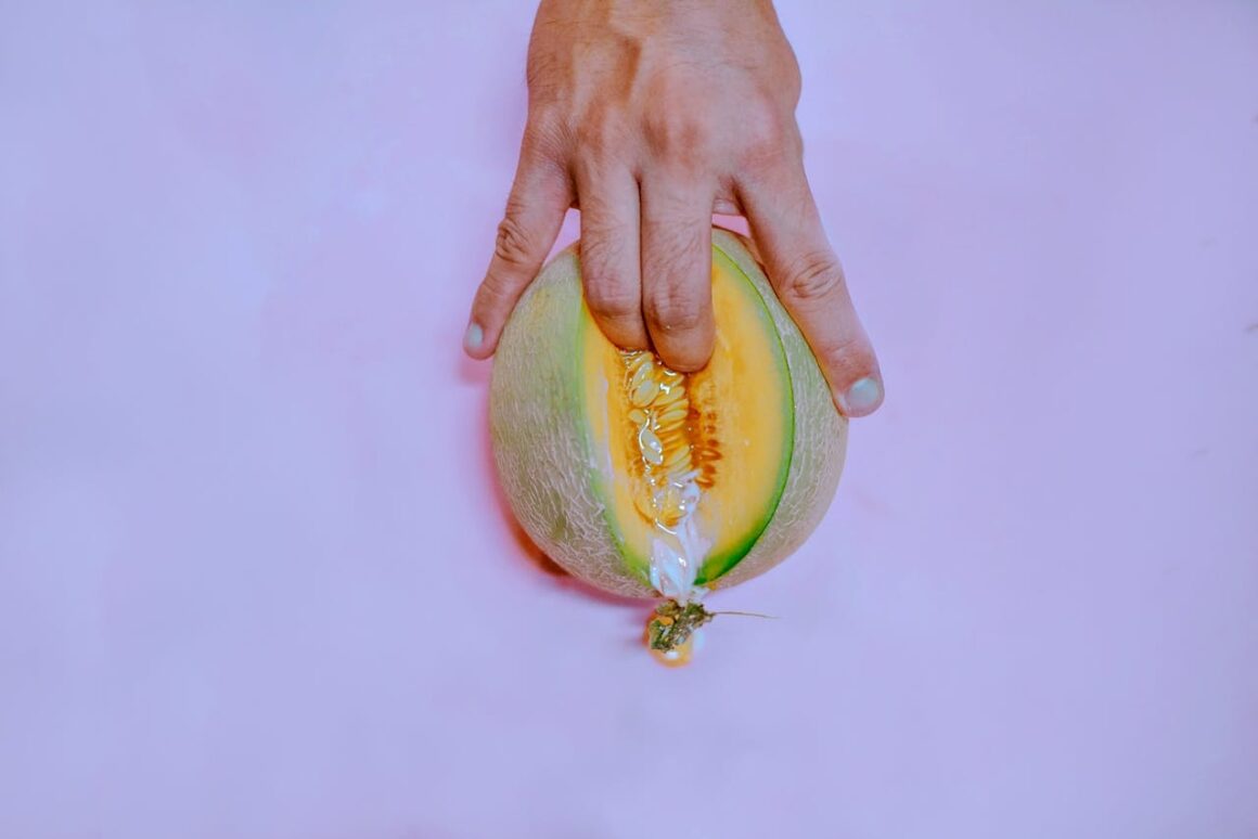 person sticking their fingers inside a melon fruit