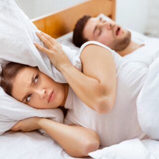 irritated woman lying beside a sleeping man