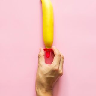 hand putting a condom on a banana on a pink background