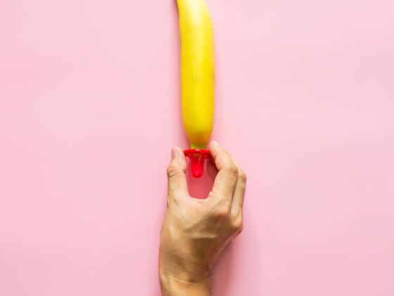 hand putting a condom on a banana on a pink background