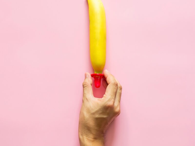 hand putting a condom on a banana on a pink background