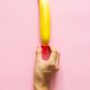 hand putting a condom on a banana on a pink background