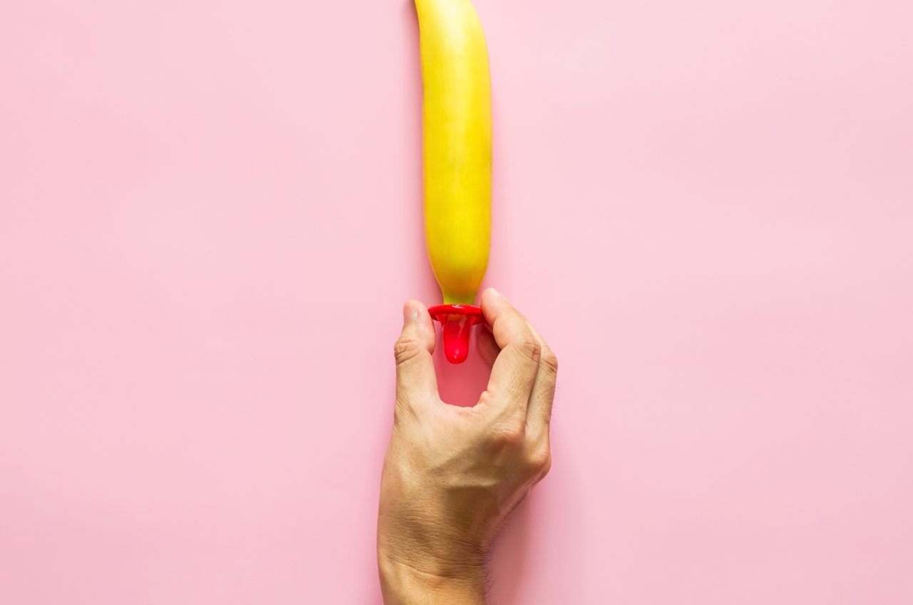 hand putting a condom on a banana on a pink background