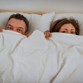 couple in bed hiding under a blanket