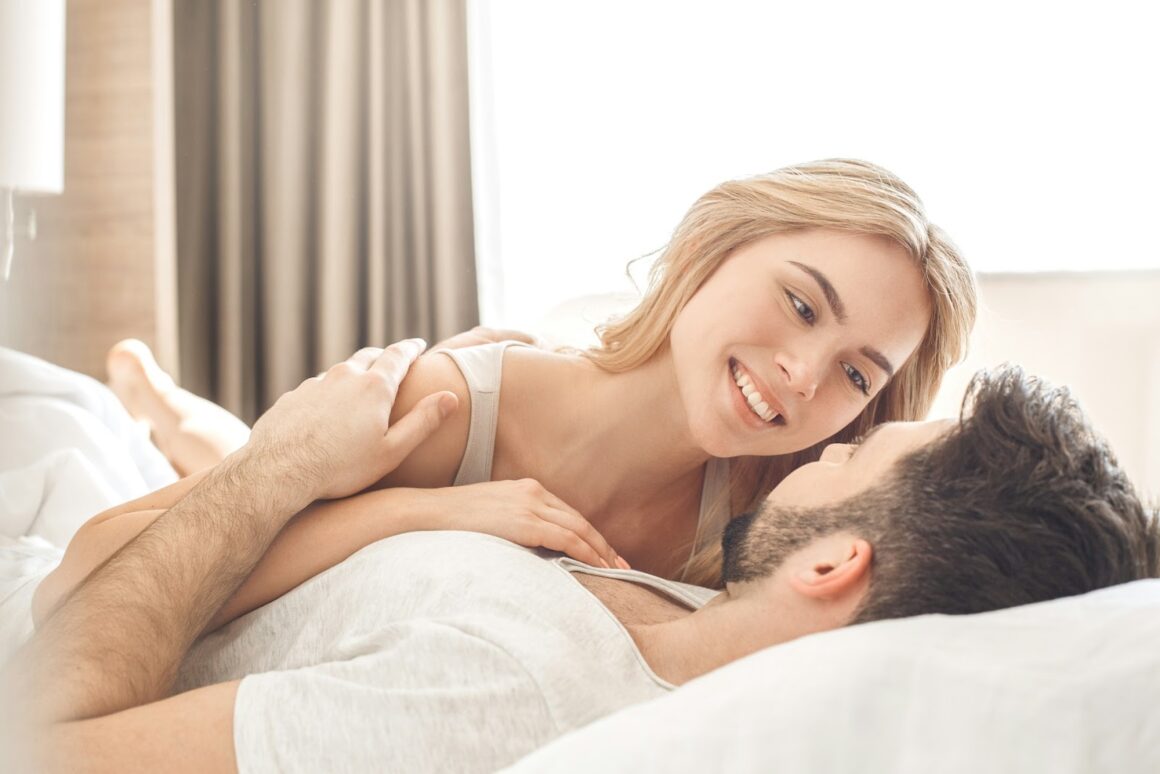 A girlfriend and boyfriend smile and giggle in bed together