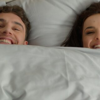 happy smiling couple under a duvet in bed