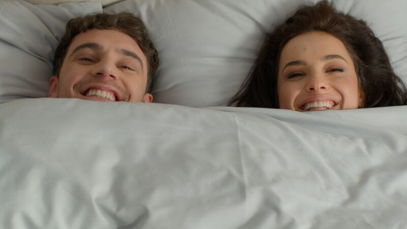 happy smiling couple under a duvet in bed
