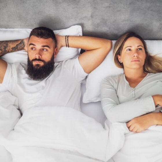couple lying apart in bed, visibly frustrated and upset