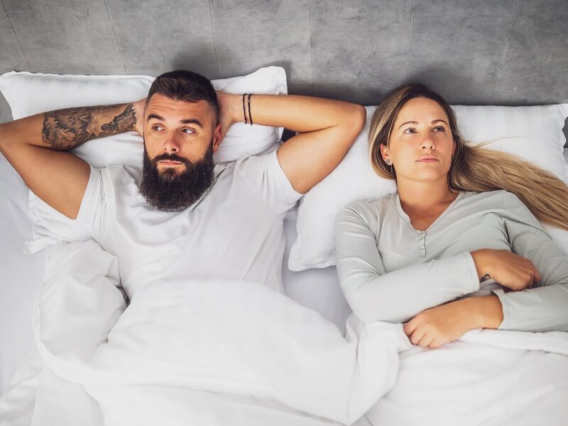 couple lying apart in bed, visibly frustrated and upset