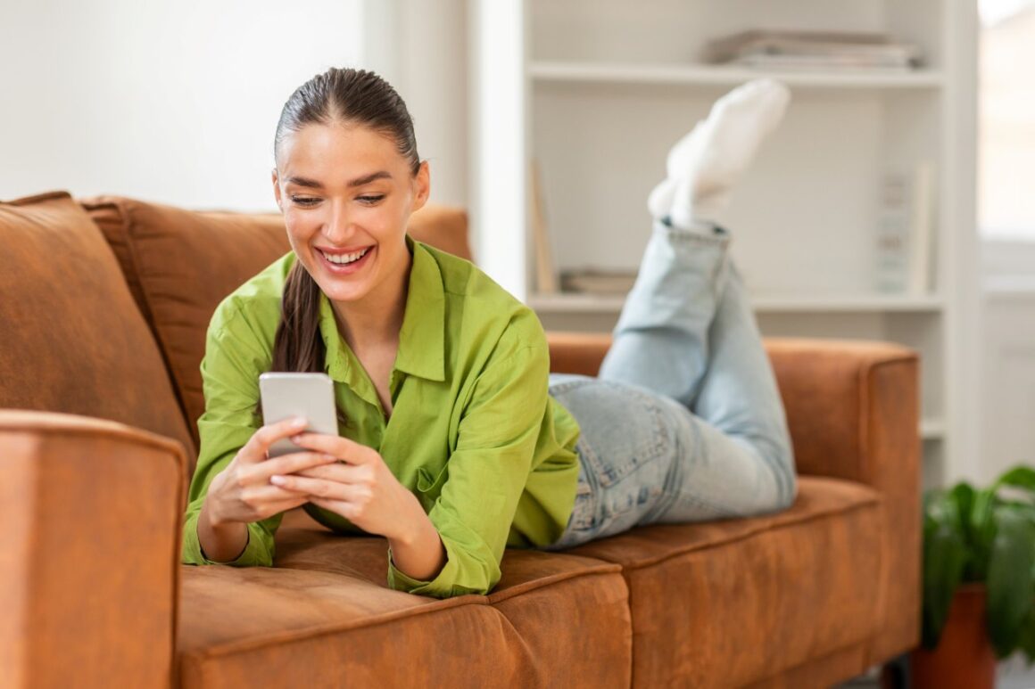 A woman is laying down on a couch while using a smart phone