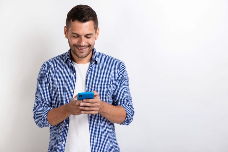 Attractive man standing holding a smartphone in his hands and looking at the screen