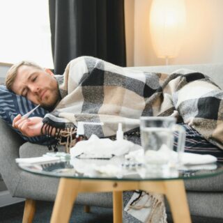 Sick bearded man who has bad cold or seasonal flu lying on couch at home