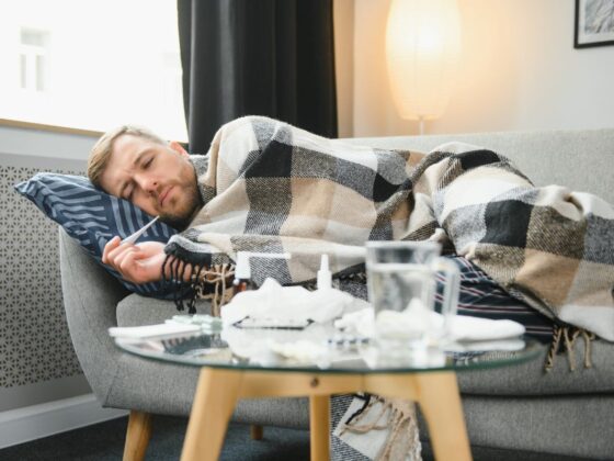 Sick bearded man who has bad cold or seasonal flu lying on couch at home