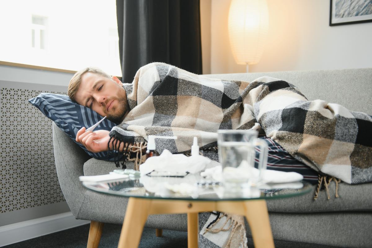 Sick bearded man who has bad cold or seasonal flu lying on couch at home
