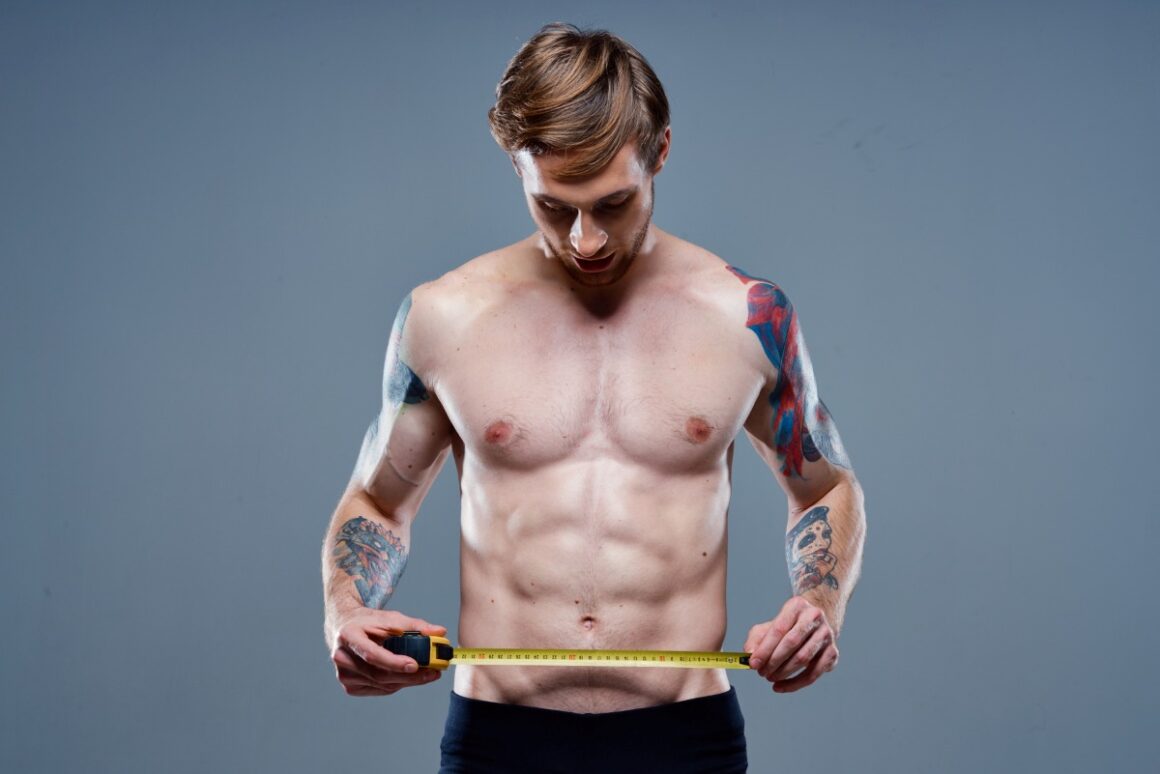 shirtless man with tattoo holding tape measure around his waist
