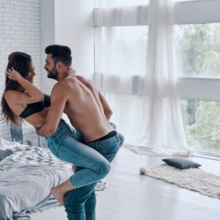 shirtless man carrying semi-dressed attractive woman while standing in the bedroom