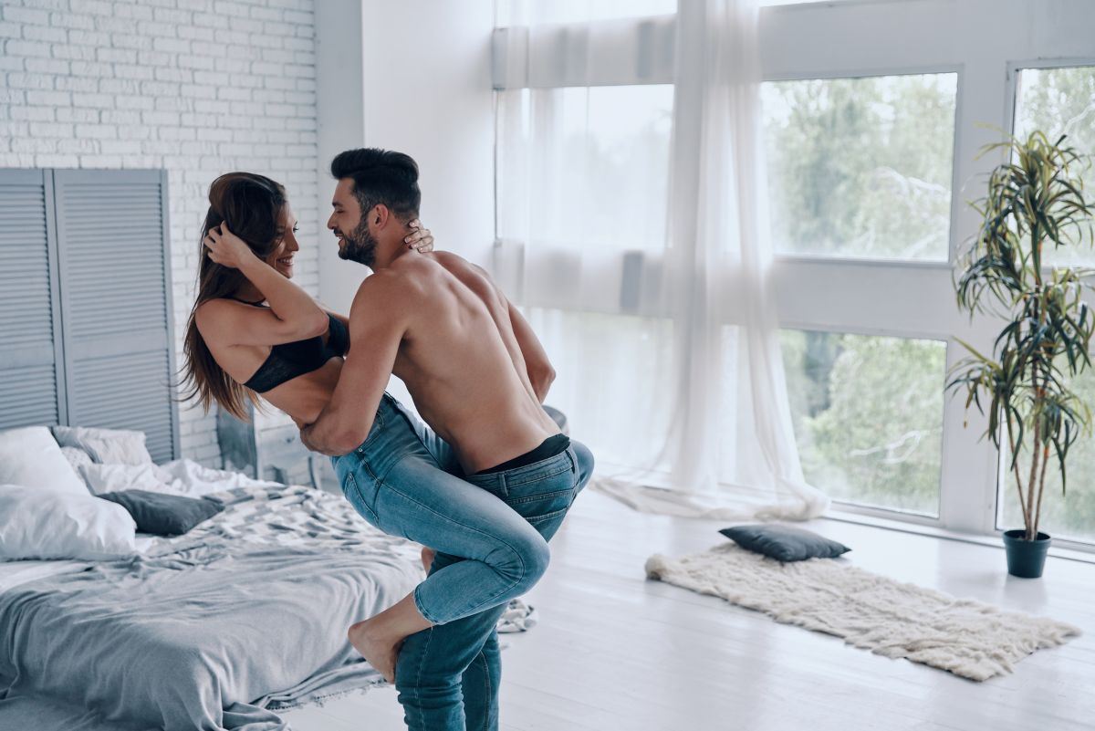 shirtless man carrying semi-dressed attractive woman while standing in the bedroom